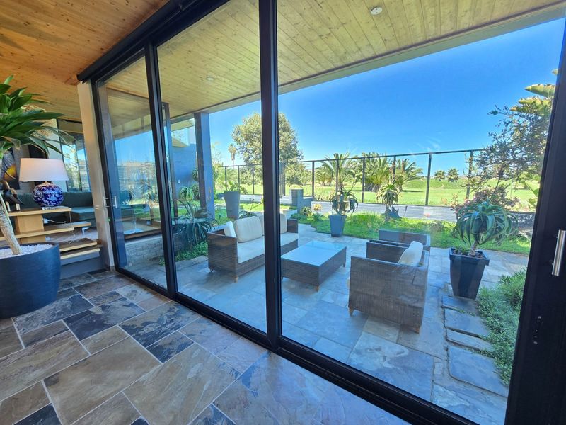 A modern indoor-outdoor transition space featuring large sliding glass doors, natural stone flooring, and a timber-clad ceiling overlooking a landscaped garden.