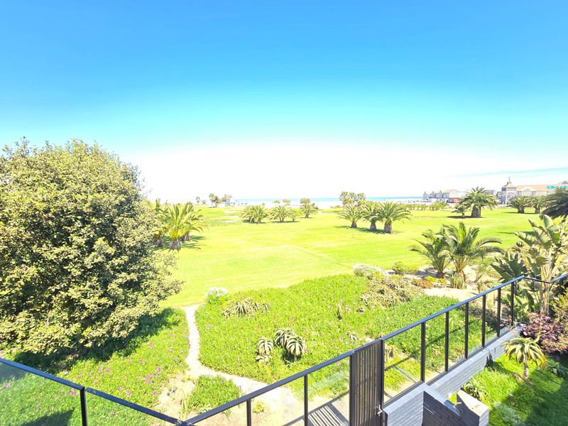 Elevated view overlooking a landscaped garden, palm trees, and coastal scenery from a balcony with a modern glass balustrade.