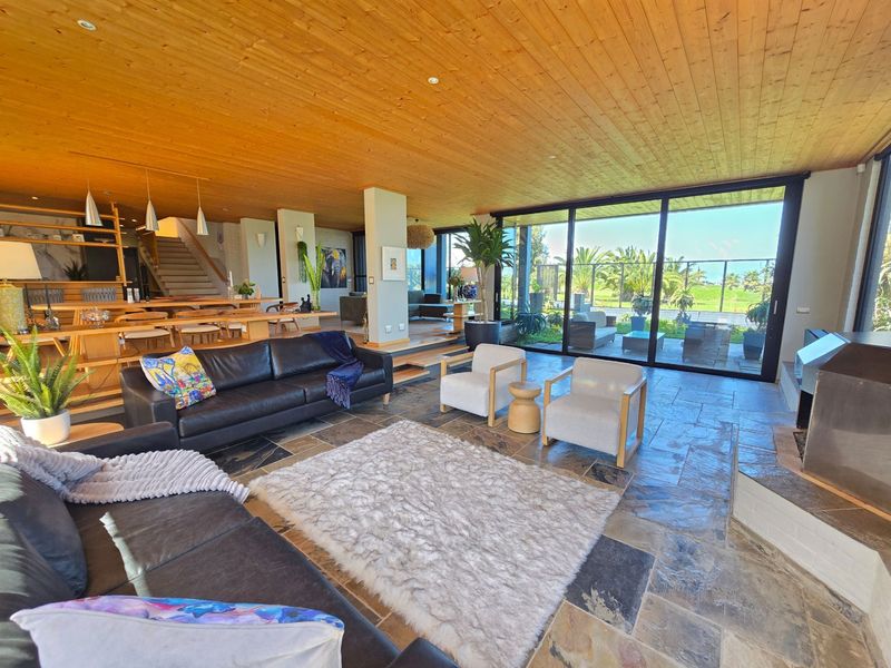 Spacious open-plan living area featuring natural timber ceilings, slate flooring, and expansive floor-to-ceiling glass doors providing seamless indoor-outdoor flow.
