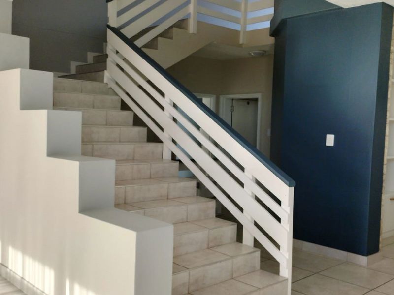A bright hallway featuring a tiled staircase with a white railing and a dark blue accent wall with built-in shelving.
