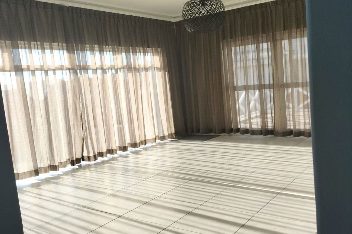 A bright, empty living room featuring neutral tiled flooring and large sliding glass doors that provide ample natural light.