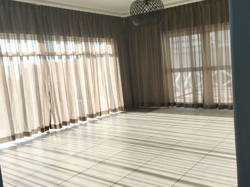 A bright, empty living room featuring neutral tiled flooring and large sliding glass doors that provide ample natural light.
