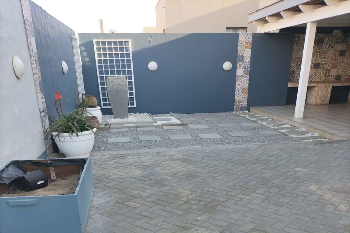 A low-maintenance rear courtyard featuring paved areas, gravel landscaping, decorative wall accents, and a built-in braai area under a covered patio.