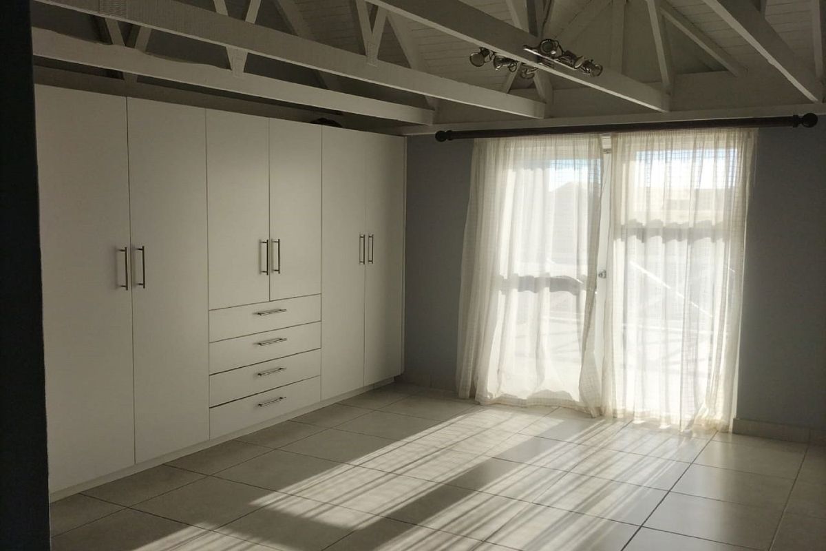 Spacious bedroom featuring built-in cupboards, tiled flooring, and exposed roof trusses, with direct access to an outdoor area through a sliding glass door.