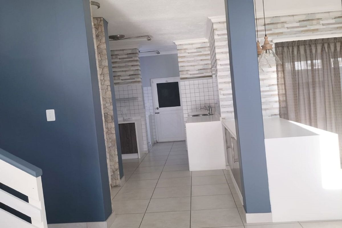 A bright, open-plan kitchen area featuring tiled flooring, modern cabinetry, and decorative stone-cladding pillars, offering a clean and functional space.