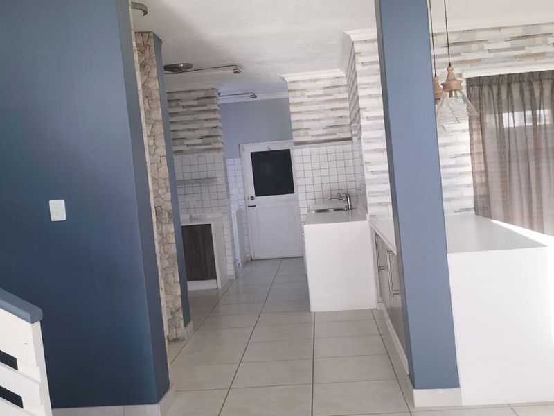 A bright, open-plan kitchen area featuring tiled flooring, modern cabinetry, and decorative stone-cladding pillars, offering a clean and functional space.