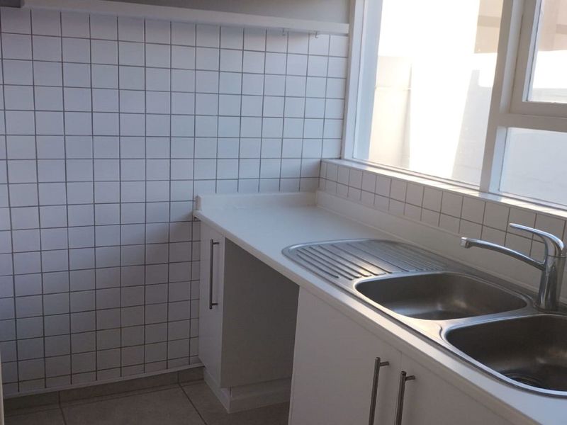 A clean and functional scullery area featuring a double bowl stainless steel sink, white cabinetry, and tiled splashbacks.