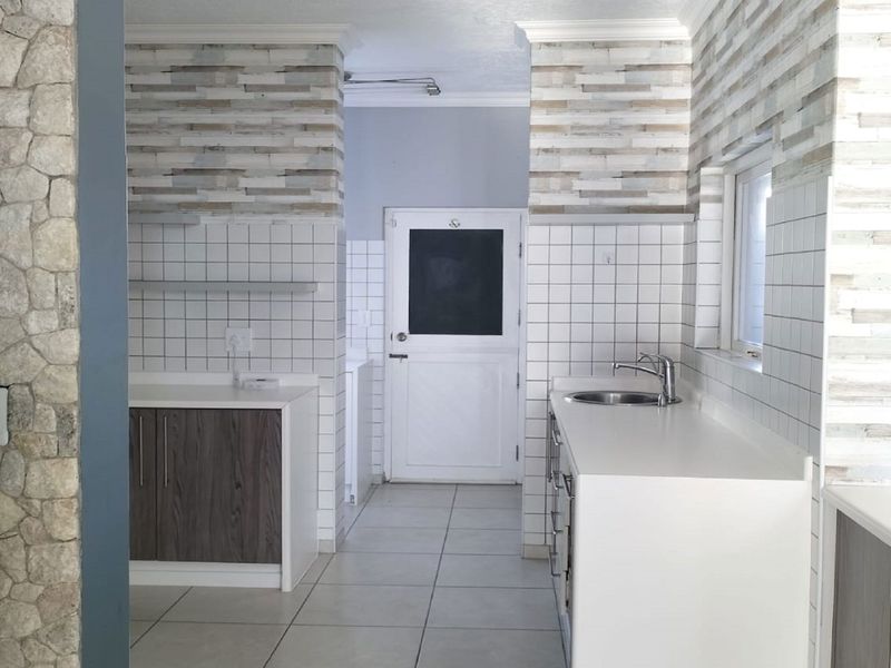 A clean, functional kitchen featuring tiled surfaces, built-in cabinetry, a stainless steel sink, and a decorative stone veneer accent wall.