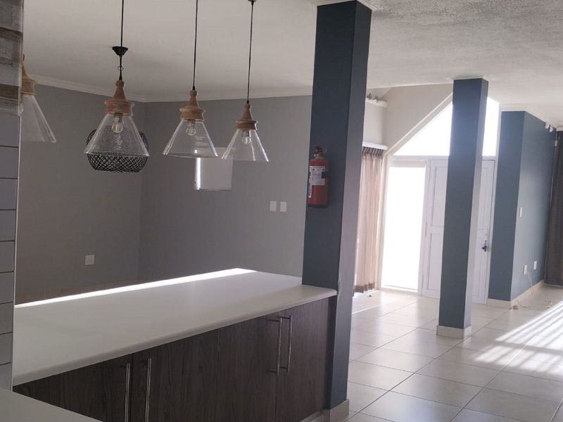 An open-plan living and kitchen area featuring modern pendant lighting, tiled flooring, and structural columns, offering a bright and versatile layout.