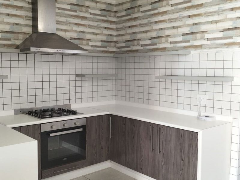 Modern kitchen featuring dark wood-look cabinetry, white stone countertops, a gas cooktop with extractor fan, and a decorative tiled backsplash.