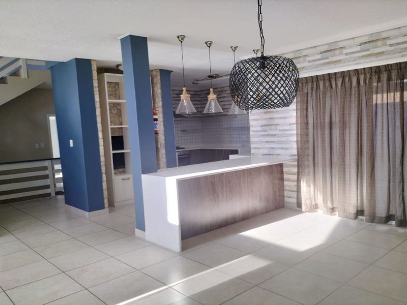 Open-plan living area featuring a breakfast bar, stone accent wall, tiled flooring, and a staircase, creating a modern and functional flow.