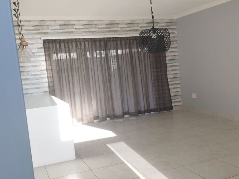 An open-plan living area featuring neutral tiled flooring, a textured feature wall, and large sliding glass doors providing natural light.
