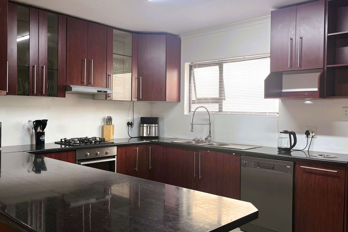A functional kitchen featuring dark wood cabinetry, granite countertops, a gas hob, an electric oven, and an integrated dishwasher.