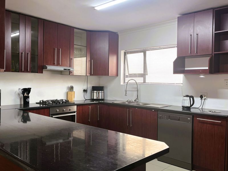A functional kitchen featuring dark wood cabinetry, granite countertops, a gas hob, an electric oven, and an integrated dishwasher.