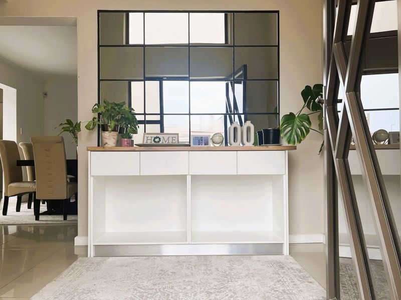 A bright and welcoming entrance hall featuring a modern built-in console unit and a large decorative grid-pattern wall mirror.