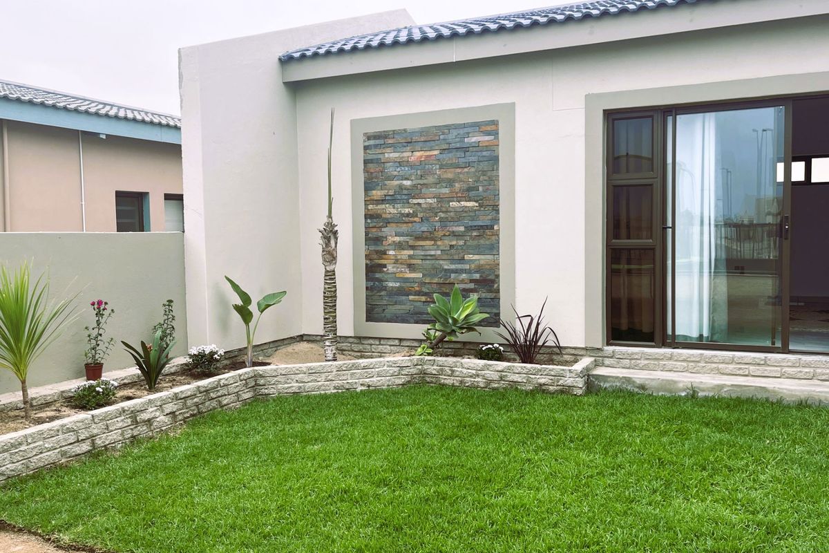 A well-maintained rear garden area featuring a stone-clad feature wall, a manicured lawn, and a sliding glass door providing access to the interior.