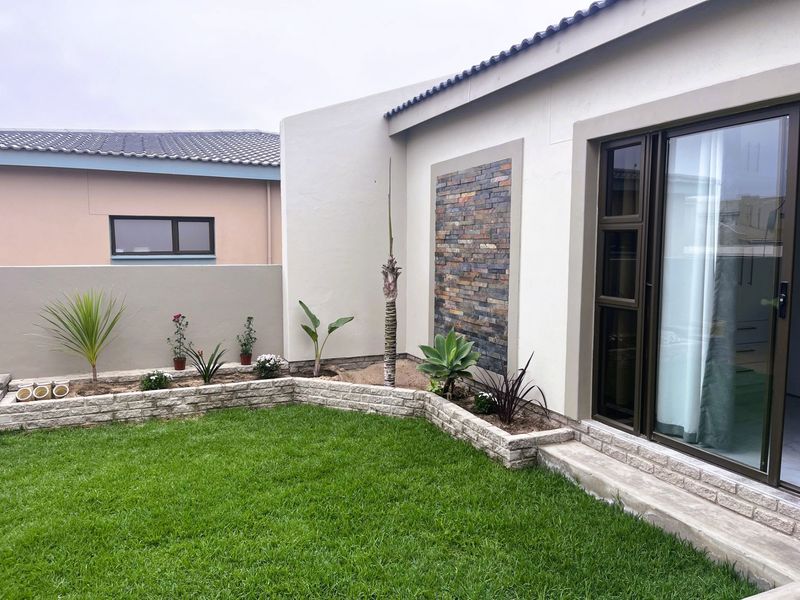 A well-maintained rear garden featuring a stone-clad feature wall, raised garden beds, and sliding glass door access to the home.
