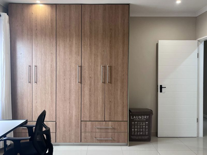A bedroom featuring modern wood-finish built-in cupboards, neutral tiled flooring, and recessed ceiling lighting.