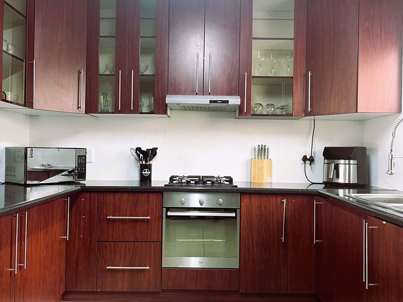 A well-maintained kitchen featuring dark wood cabinetry, granite countertops, a built-in gas hob, oven, and extractor fan with glass-fronted display cabinets.