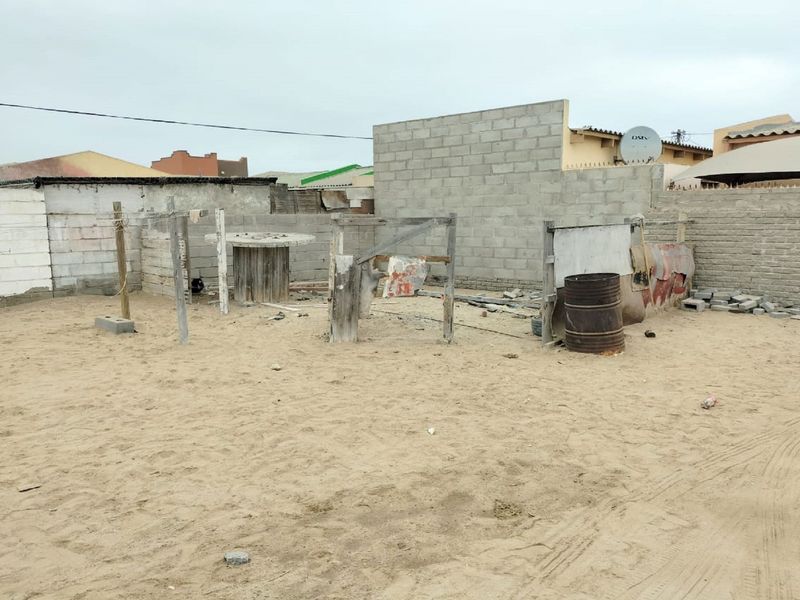 A large, undeveloped rear yard featuring sandy ground and unfinished concrete block boundary walls, offering significant potential for landscaping and outdoor improvement.