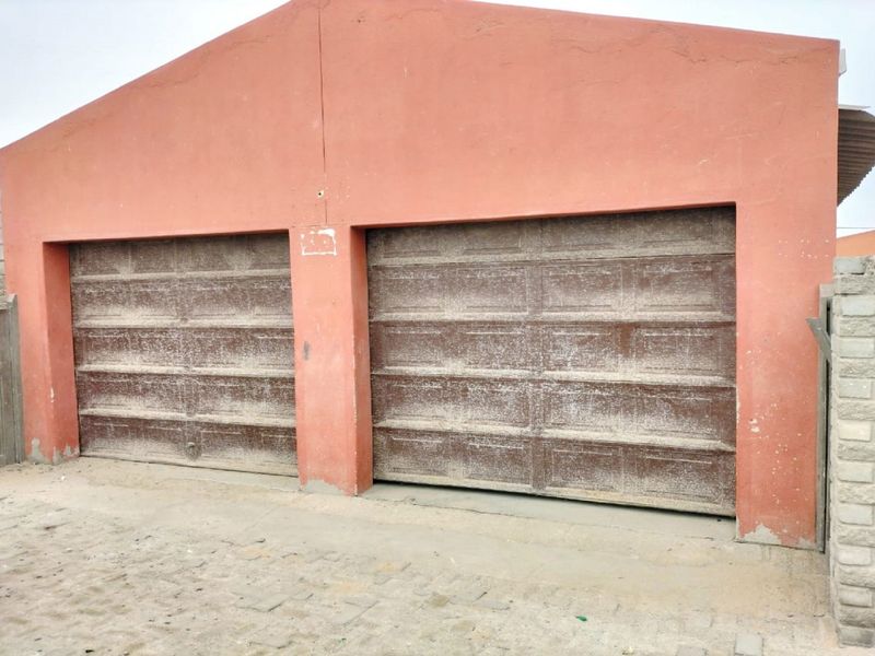 A detached double garage featuring weathered brown sectional doors and a terracotta-colored masonry facade.