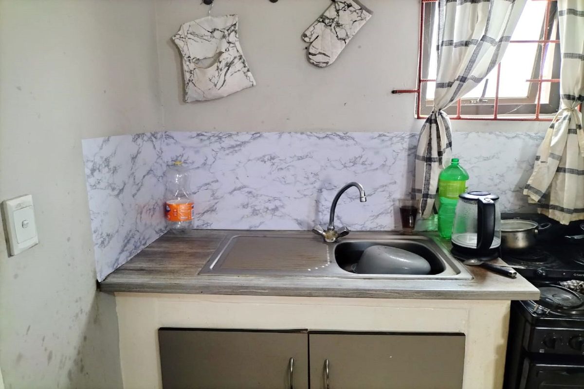 A compact kitchen area featuring a stainless steel sink, laminate countertop, and base cabinetry with visible wall wear and dated finishes.