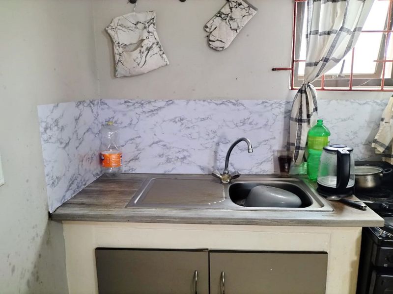 A compact kitchen area featuring a stainless steel sink, laminate countertop, and base cabinetry with visible wall wear and dated finishes.