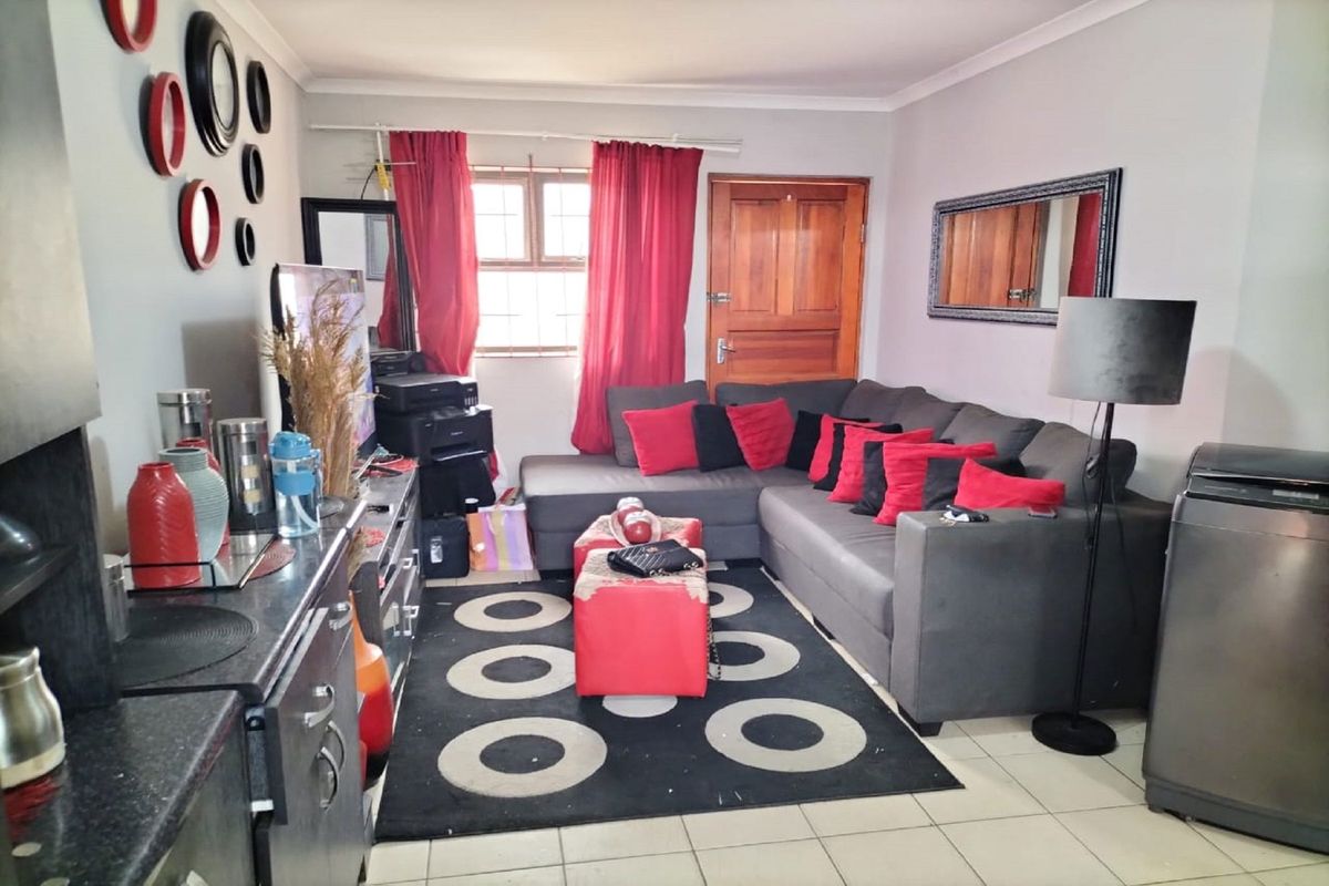 A functional living room featuring tiled flooring, a timber entrance door, and a window with security bars, offering a practical and accessible living space.