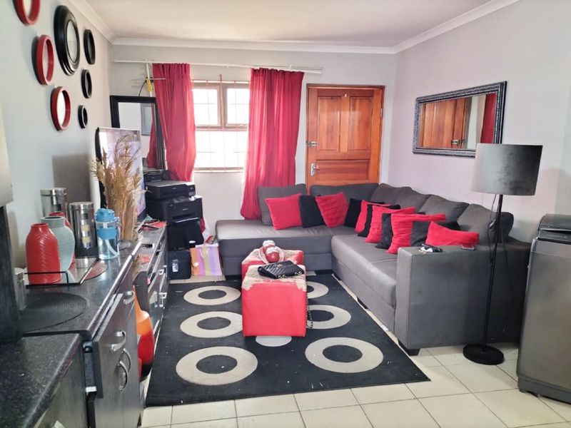A functional living room featuring tiled flooring, a timber entrance door, and a window with security bars, offering a practical and accessible living space.