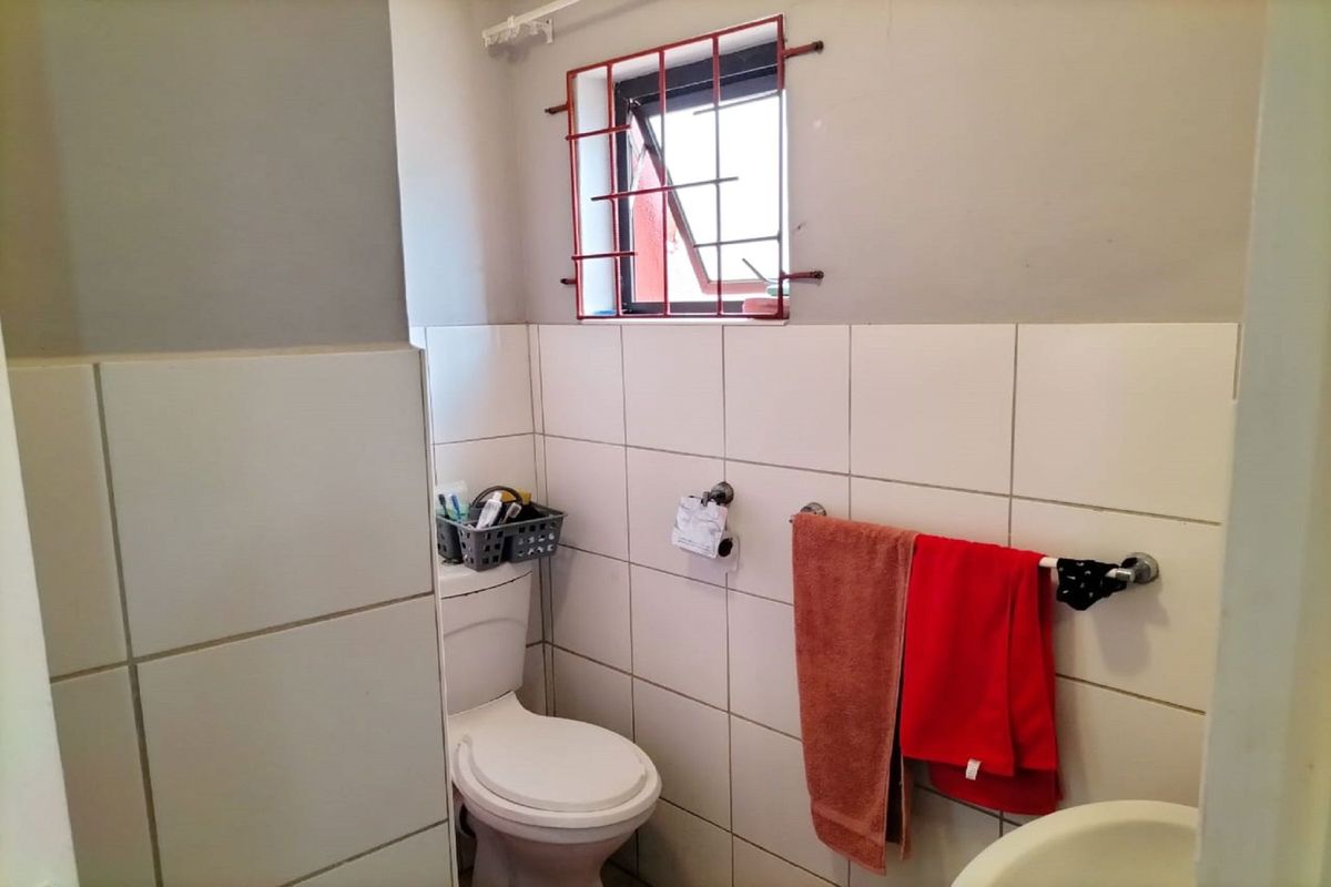 A compact bathroom featuring a standard toilet, basin, and tiled walls with security bars on the window.