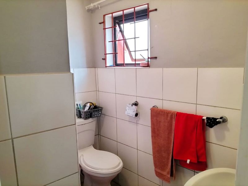 A compact bathroom featuring a standard toilet, basin, and tiled walls with security bars on the window.