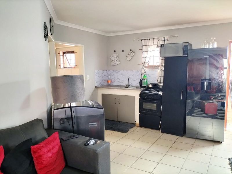 Open plan living area featuring a compact kitchen with built-in cabinetry, tiled flooring, and a freestanding stove.