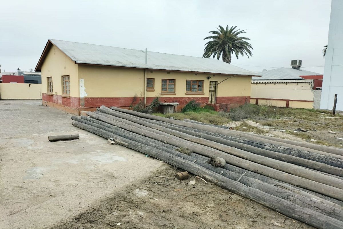 Rear view of a single-story commercial building featuring a corrugated metal roof, brick base, and paved yard area requiring maintenance.