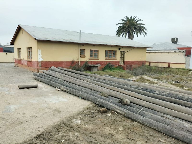 Rear view of a single-story commercial building featuring a corrugated metal roof, brick base, and paved yard area requiring maintenance.