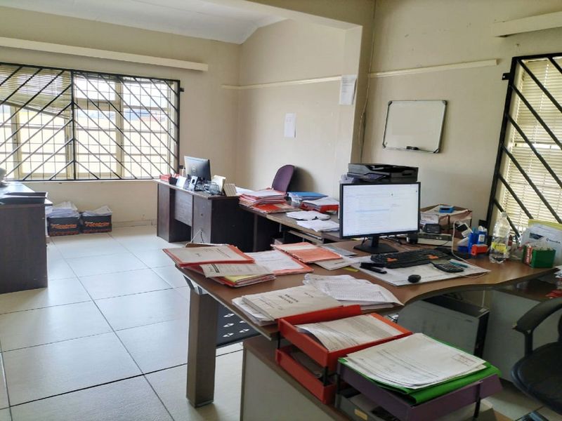 A functional office space featuring tiled flooring and large windows with security bars, providing ample natural light for a professional work environment.