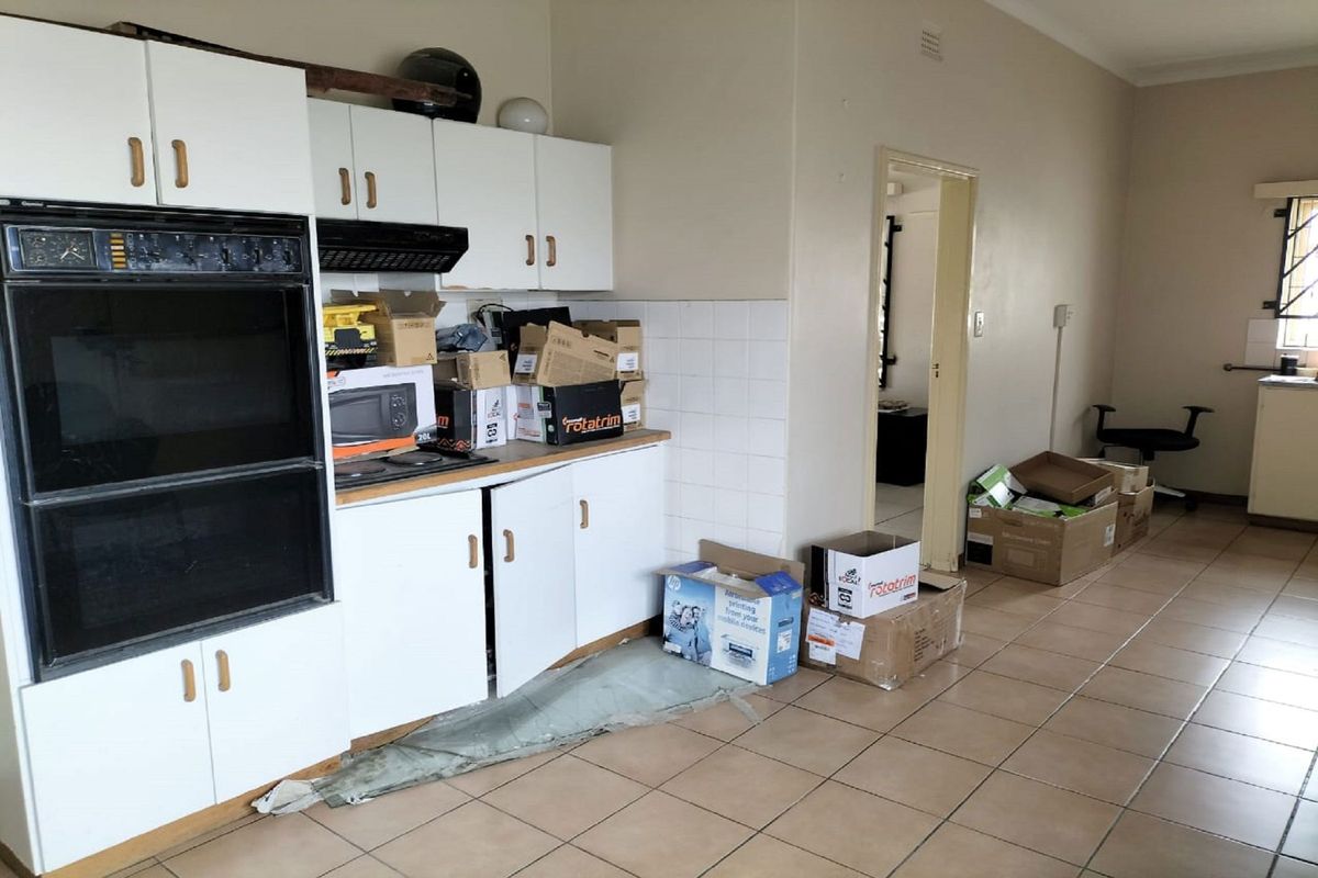 A dated kitchen area featuring built-in double ovens, white cabinetry, and tiled flooring, currently used as a storage space.