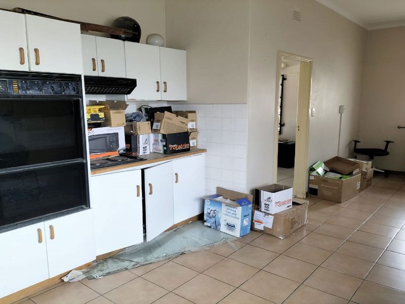 A dated kitchen area featuring built-in double ovens, white cabinetry, and tiled flooring, currently used as a storage space.