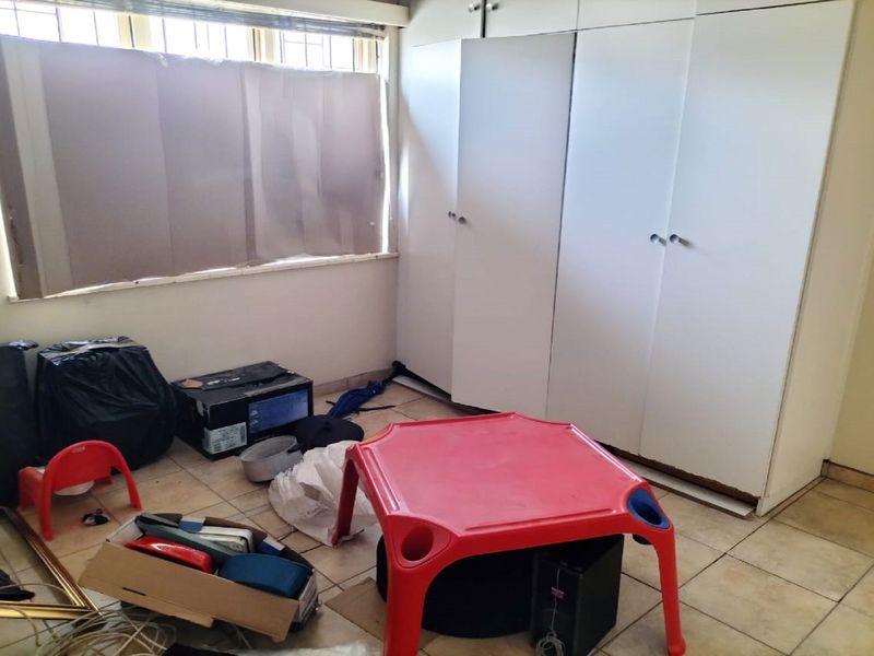 A bedroom featuring built-in cupboards, tiled flooring, and security bars on the windows, currently in need of maintenance and cosmetic updates.