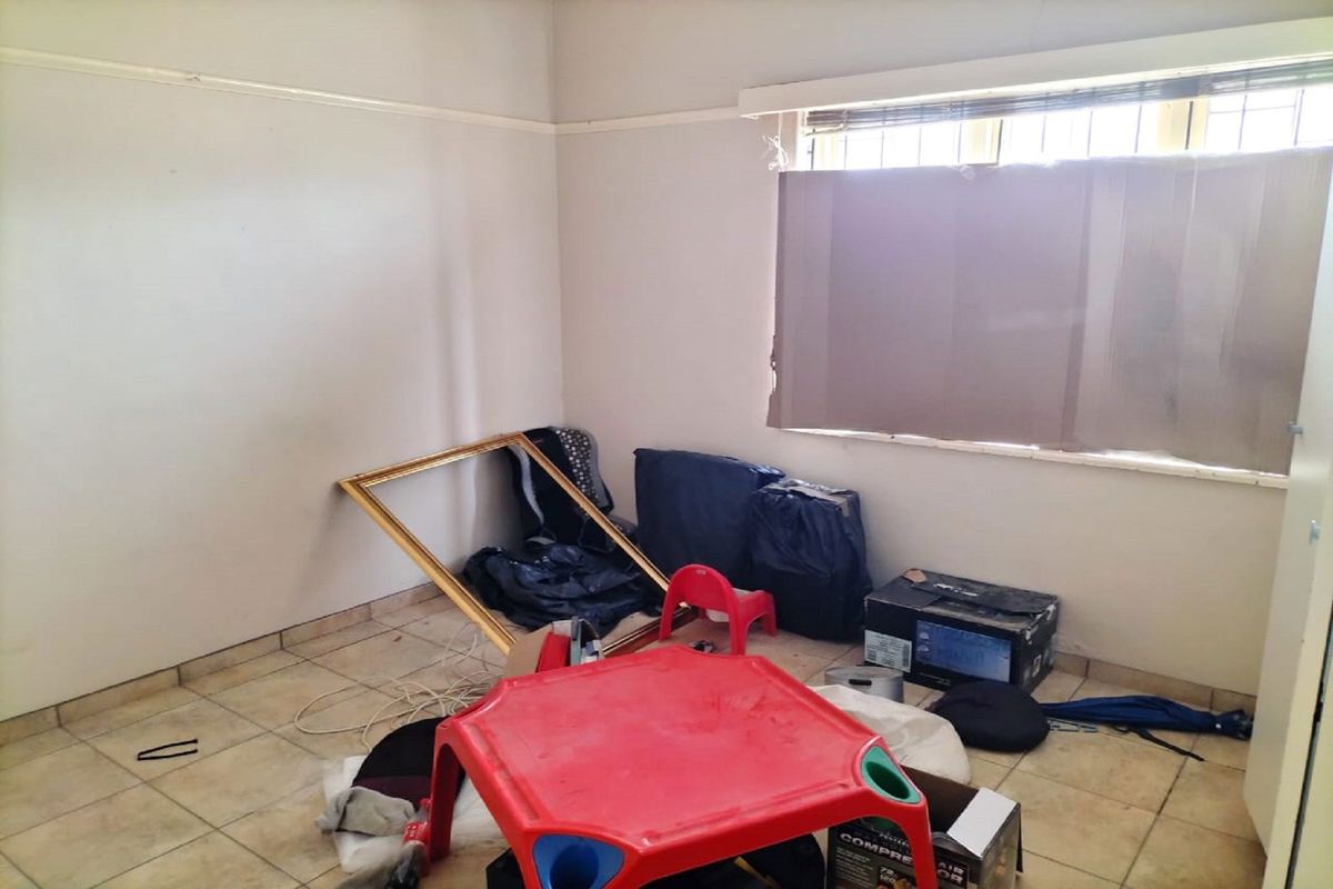 A vacant bedroom featuring tiled flooring, a window with security bars, and a picture rail, requiring cosmetic updates to improve its overall condition.