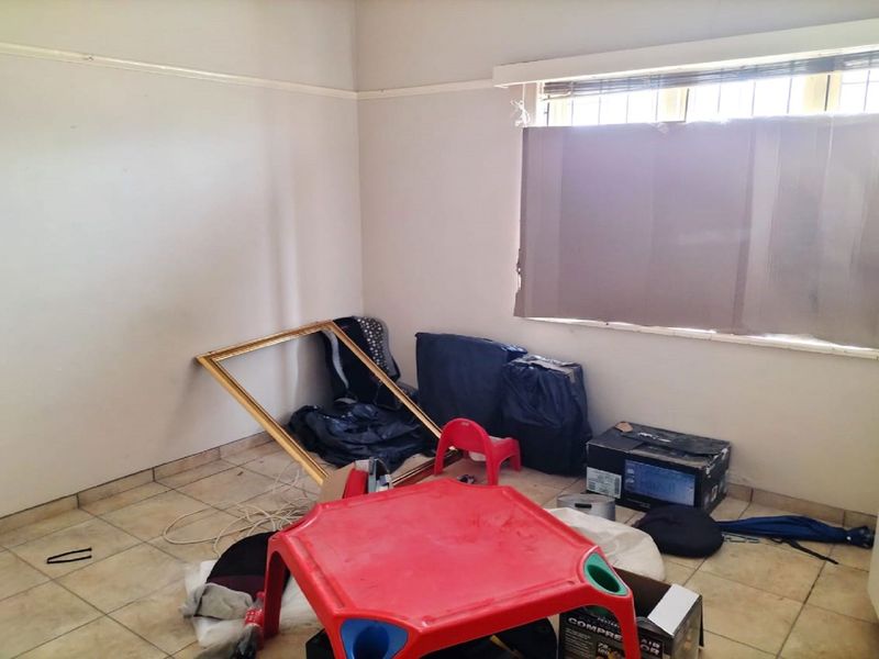A vacant bedroom featuring tiled flooring, a window with security bars, and a picture rail, requiring cosmetic updates to improve its overall condition.