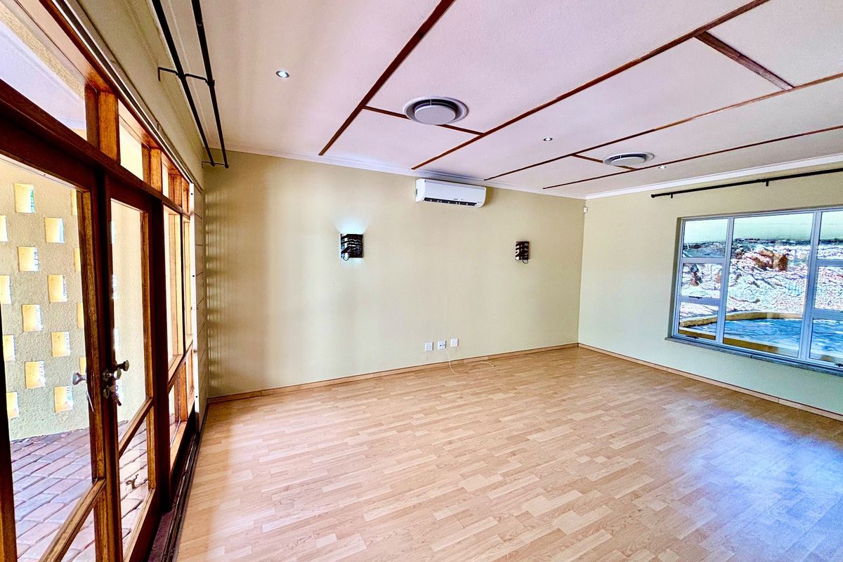 A bright, empty living room featuring laminate flooring, split-system air conditioning, and large timber-framed glass doors leading to an outdoor area.