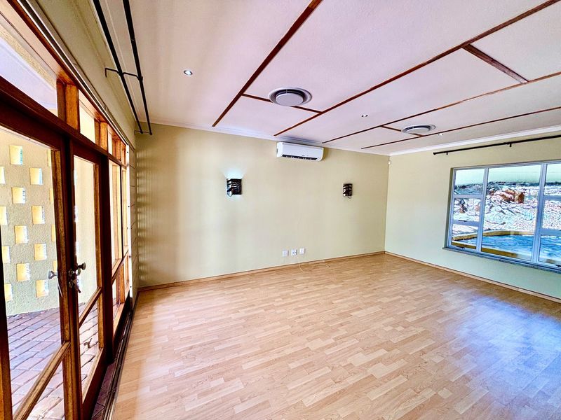 A bright, empty living room featuring laminate flooring, split-system air conditioning, and large timber-framed glass doors leading to an outdoor area.
