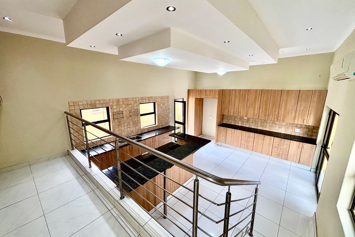 Spacious split-level kitchen featuring extensive built-in cabinetry, granite countertops, tiled flooring, and modern recessed ceiling lighting in an open-plan layout.