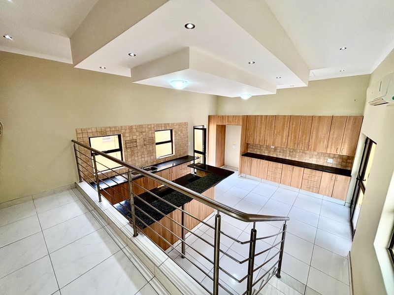 Spacious split-level kitchen featuring extensive built-in cabinetry, granite countertops, tiled flooring, and modern recessed ceiling lighting in an open-plan layout.