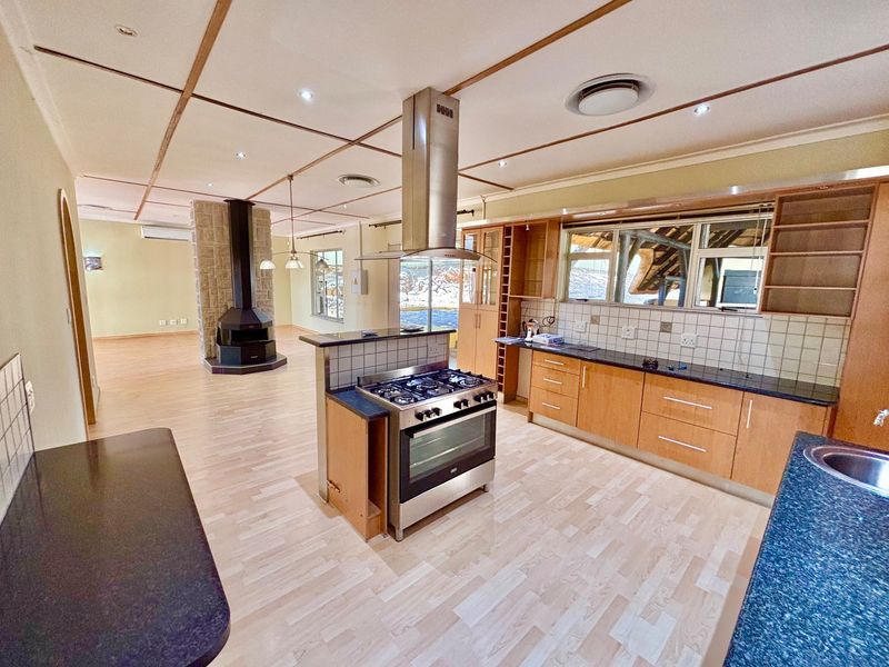 Spacious open-plan kitchen and living area featuring a central gas stove, stone fireplace, and light wood-look laminate flooring throughout.