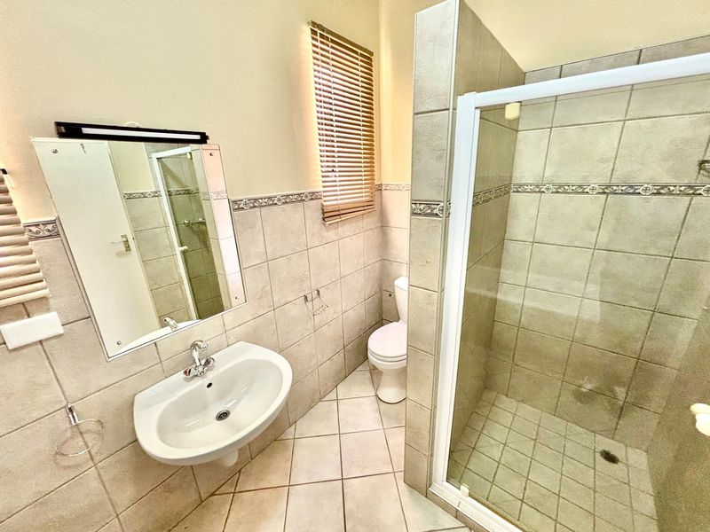 A functional bathroom featuring a wall-mounted basin, a tiled shower enclosure, and a toilet, finished with neutral wall tiles and floor tiling.