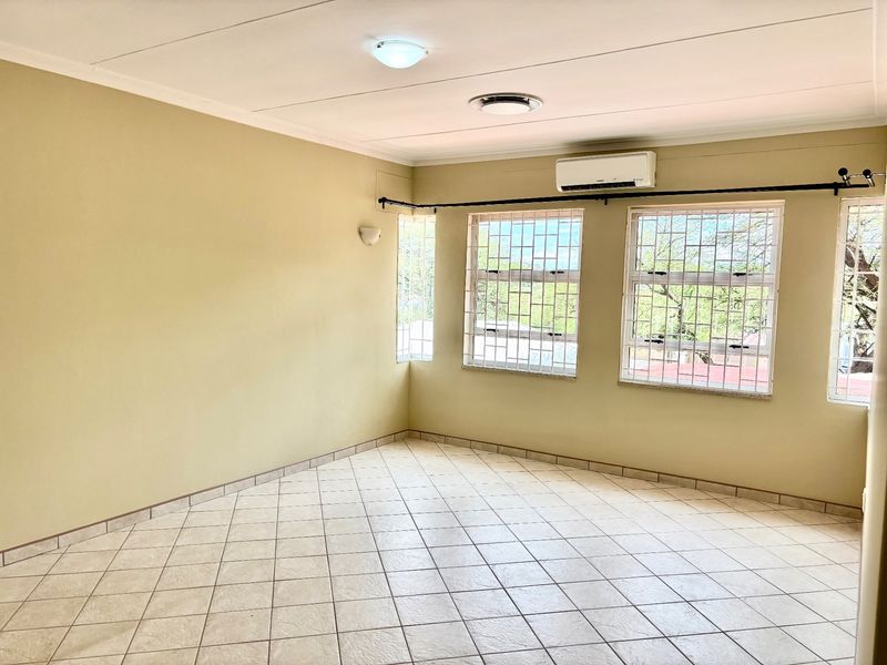 An empty living room featuring tiled flooring, an air conditioning unit, and windows fitted with security bars.