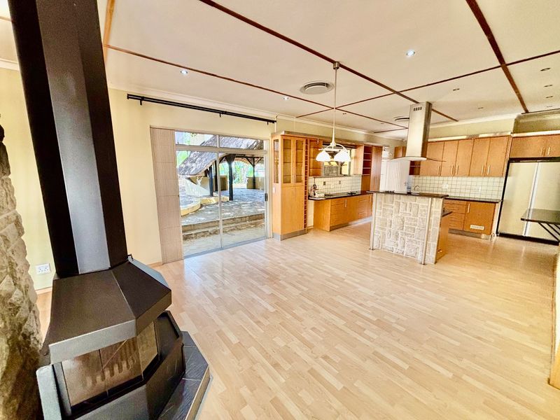Spacious open-plan living and kitchen area featuring light wood laminate flooring, a central stone-clad island, and a modern freestanding fireplace with direct patio access.