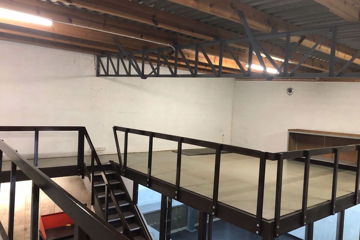 Industrial open-plan mezzanine level featuring exposed timber roof trusses, steel structural elements, and a functional staircase, suitable for office or storage use.