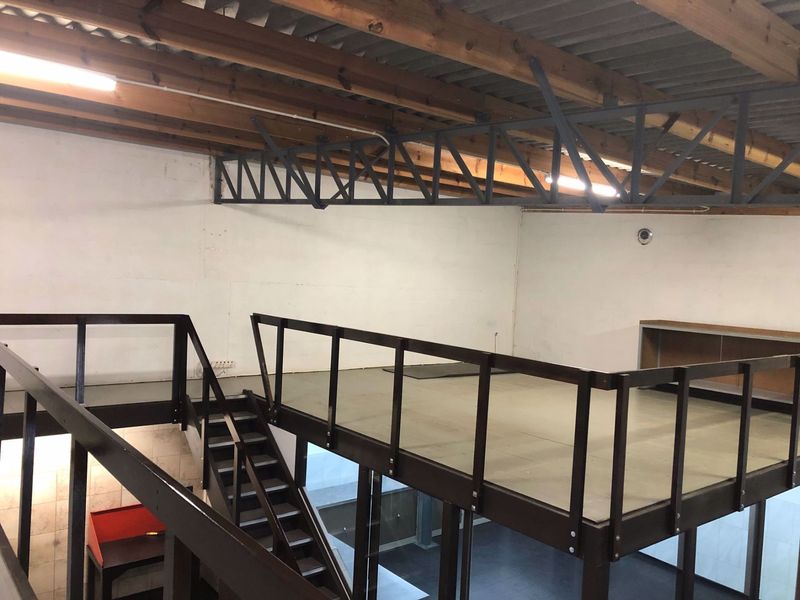 Industrial open-plan mezzanine level featuring exposed timber roof trusses, steel structural elements, and a functional staircase, suitable for office or storage use.